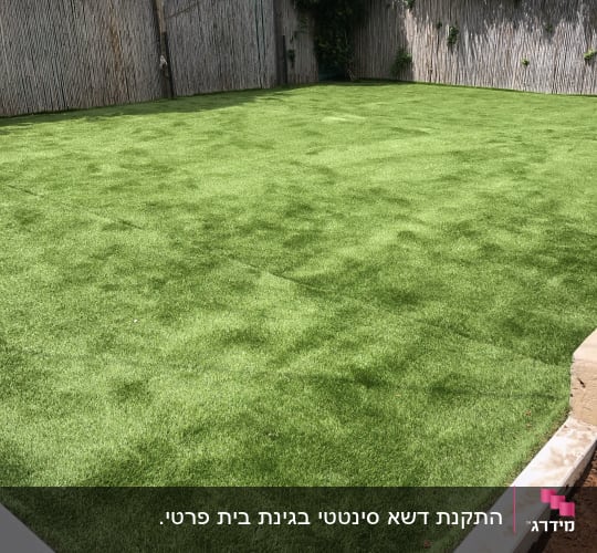 דשא ירוק מוקף בגדר עץ גבוהה